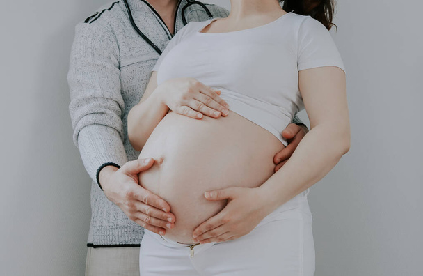 Un homme tient le ventre d'une femme enceinte avec les mains sur un fond blanc, vue latérale rapprochée. - Photo, image
