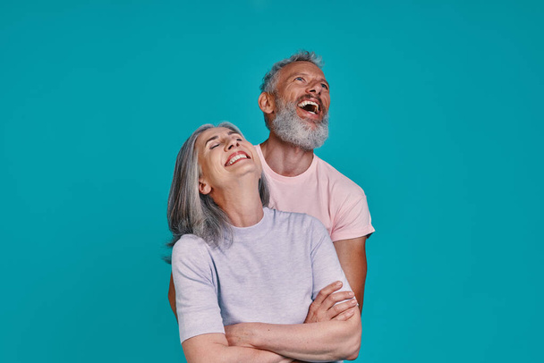 Heureux couple de personnes âgées coller et rire tout en se tenant ensemble sur fond bleu - Photo, image