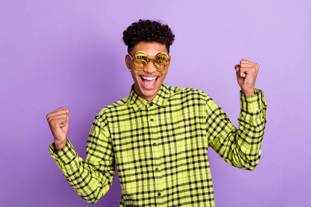 Photo portrait of guy funky wearing golden glasses with dollar sign gesturing like winner isolated on pastel purple color background - Фото, изображение