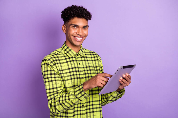 Portrait of attractive cheerful brunet guy holding in hands using device ebook isolated over violet purple color background - Φωτογραφία, εικόνα