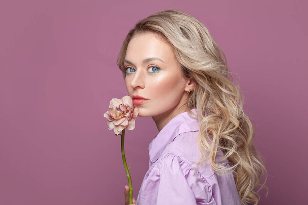 Fashion beauty portret van mooie vrouw met een gezonde huid met bloemen in de buurt van haar gezicht op felroze achtergrond, studio portret - Foto, afbeelding