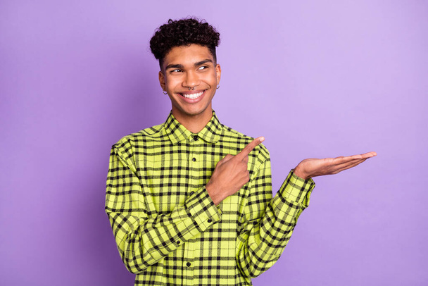 Portrait of attractive cheerful guy holding on palm demonstrating copy space isolated over violet purple color background - Fotoğraf, Görsel