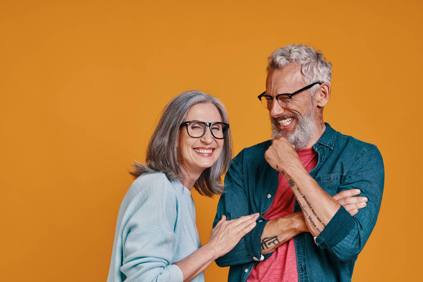 Happy senior couple smiling while standing together against orange background - Фото, зображення