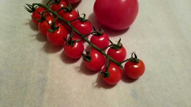 dwa duże pomidory i pomidory wiśniowe na gałęziach z bliska na beżowym tle - Materiał filmowy, wideo