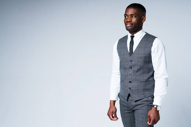 Handsome african american businessman in a shirt and vest stands on a light background - Photo, image