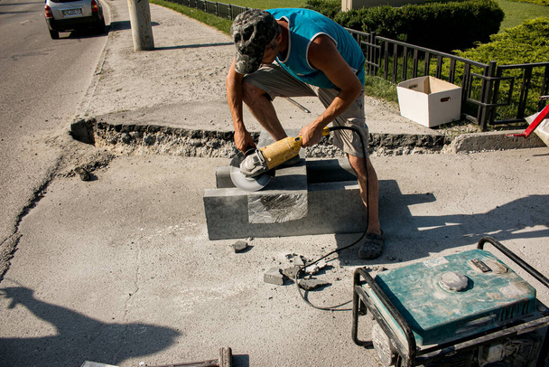 Der Prozess der Verlegung Bürgersteig Bordstein. Ein Arbeiter schneidet mit einer Kreissäge einen Betonblock. Viel Staub. - Foto, Bild