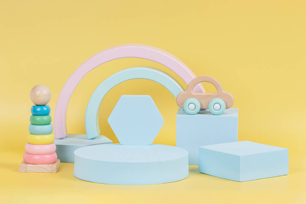Fondo de juguete de bebé niño. Composición de coloridos juguetes educativos de madera natural y formas geométricas podio, plataforma sobre fondo amarillo pastel - Foto, imagen