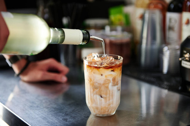 Primer plano de barista preparando una refrescante bebida helada con cafeína, vertiendo un cóctel líquido en un vaso con bebida con leche helada - Foto, Imagen