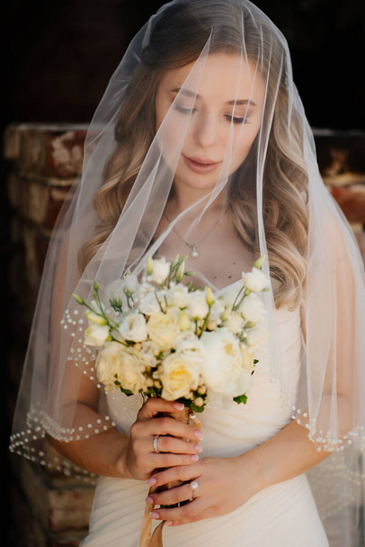 beautiful bride with long wavy hair under the veil outside with a bouquet - Φωτογραφία, εικόνα
