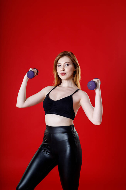 brown-haired girl in black leggings and a T-shirt goes in for sports. on a red background. - Foto, afbeelding