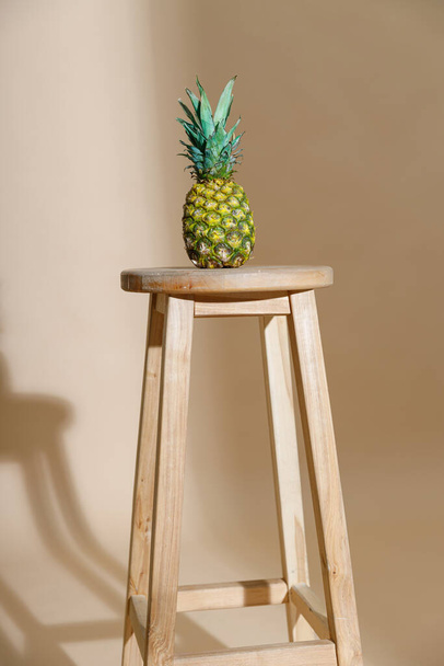 Στούντιο πλάνο νόστιμα φρέσκα ολόκληρο ανανά με φύλλα σε καρέκλα απομονώνονται σε μπεζ φόντο - Φωτογραφία, εικόνα