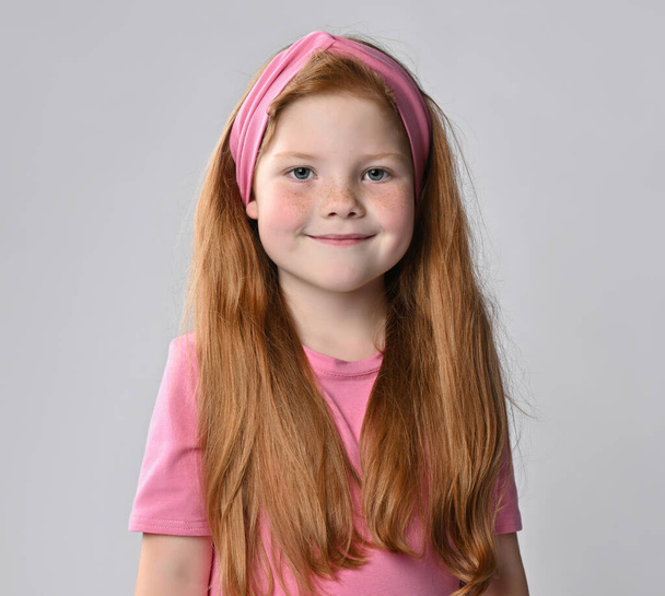 Charming red-haired girl child with folded hands under cheek studio shot - Foto, Bild