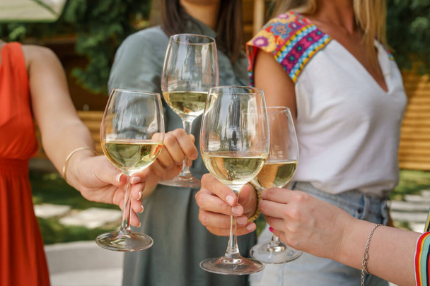 Close up on hands of unknown caucasian women holding glasses of white wine toasting and celebrating while standing outdoor - Foto, imagen