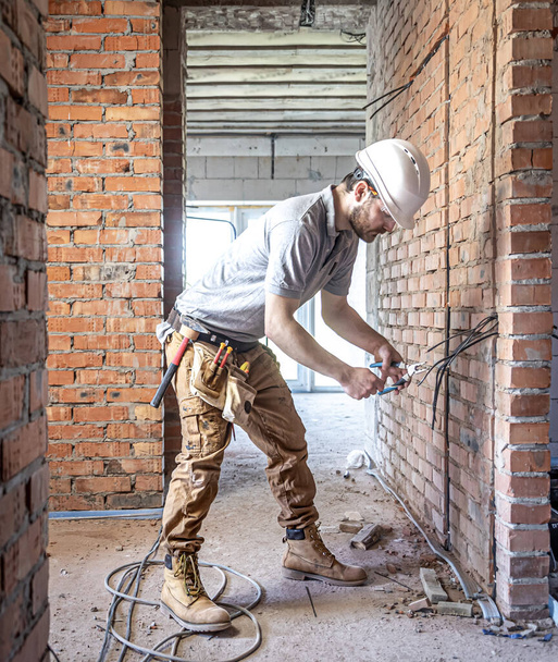 Un electricista de construcción corta un cable de voltaje durante una reparación. - Foto, Imagen