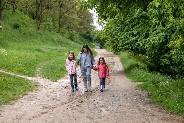 Mom and daughters are walking in the forest after rain in rubber boots in the spring. - Photo, Image