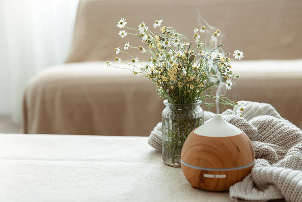 Современный масляный ароматизатор в гостиной на столе с трикотажным элементом и цветочным пространством. - Фото, изображение