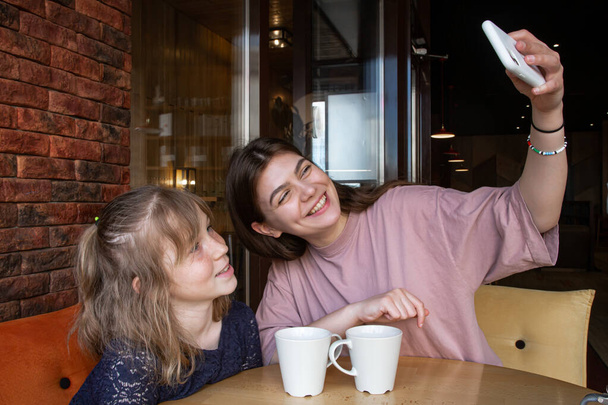 Two sisters smile and take a selfie in a cafe, over a cup of tea. - Photo, Image