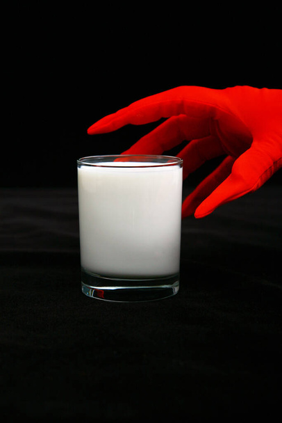 Glass of milk. A glass of milk being held by a woman's hand wearing bright red gloves. isolated on black velvet. room for text. clipping path. Natural milk in a glass on a black background. Cows Milk a transparent glass. Milk product.  - Photo, Image