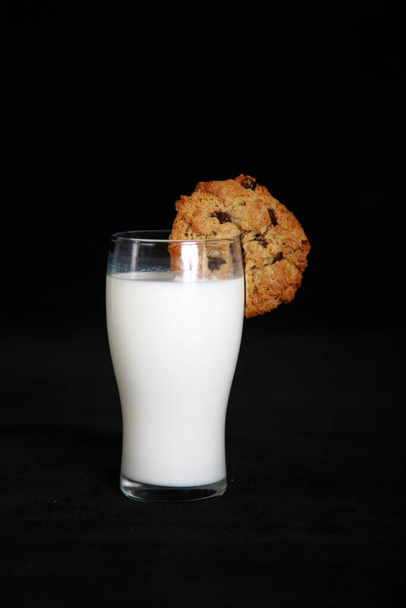 Milk and Cookies. Milk and Chocolate Chip Cookies. A retro bottle of fresh cold milk with one large chocolate chip cookie. milk bottle and cookies. good old fashioned foods and treats. Glass of milk and cookies isolated on black velvet.  - Valokuva, kuva