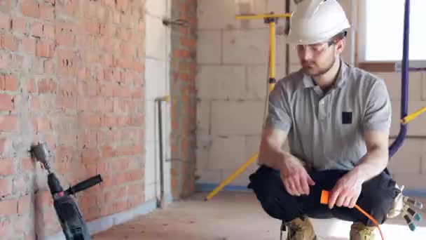 Kypärässä asuva rakennusmies kytkee poraustyökalun pistorasiaan.. - Materiaali, video