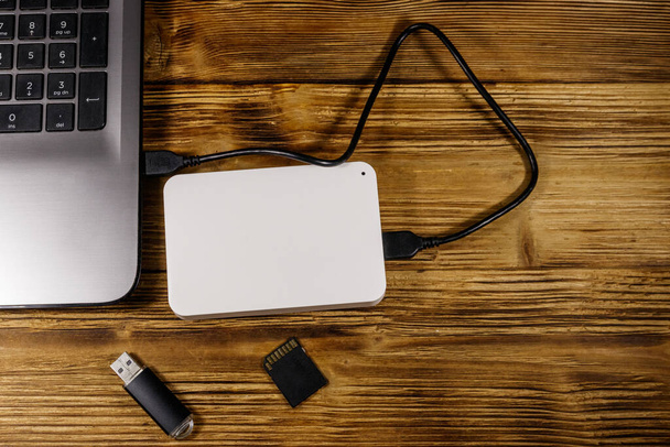 Внешний жесткий диск, подключенный к ноутбуку, SD-карте памяти и USB-флешке на деревянном столе. Вид сверху. Концепция хранения данных - Фото, изображение