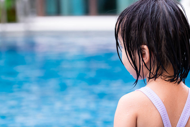 Hátsó nézet gyermek lány fürdőruhát visel a kék medencében. A kölyök nyáron vizet játszik. Gyermekbiztonsági óvintézkedések. 4-5 éves csecsemő. - Fotó, kép