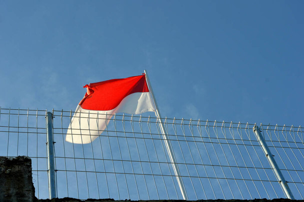Червоно-білий прапор Індонезії пурхає на залізний стовп з-за залізного дротяного паркану - Фото, зображення