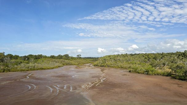 sartenes de sal con vegetación boscosa a cada lado de un cauce fangoso bajo un cielo azul nublado - Foto, Imagen