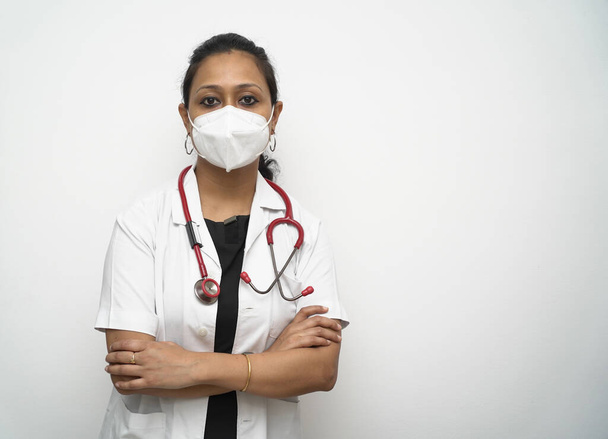 Μια νότια Ινδή γιατρός στα 30 με μάσκα λευκό παλτό και κόκκινο στηθοσκόπιο σε λευκό φόντο. - Φωτογραφία, εικόνα