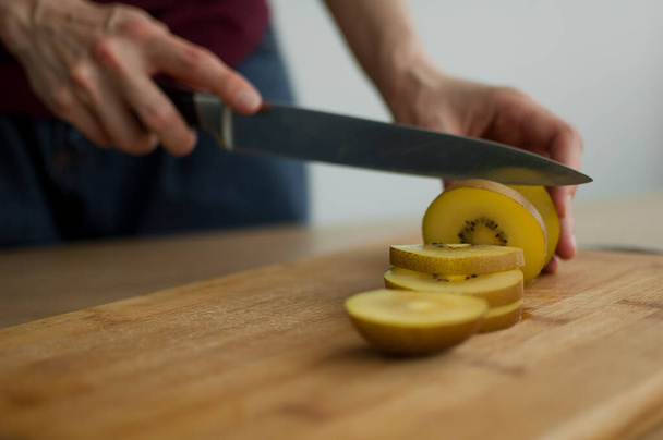 Las manos femeninas están cortando una fruta fresca madura de kiwi dorado en una tabla de madera cortada. Frutas exóticas, concepto de alimentación saludable - Foto, imagen