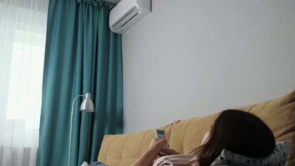 Unerkennbare Frau schaltet Klimaanlage mit Fernbedienung ein, liegt auf der Couch - Filmmaterial, Video
