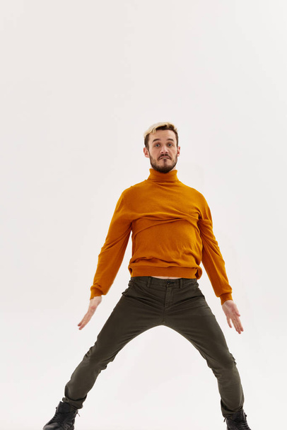 мужчина в оранжевом свитере раздвинул ноги на ширину плеч и жестикулирует руками - Фото, изображение
