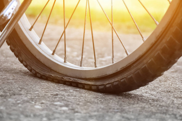 平らなタイヤを持ち、舗装された、ぼやけた背景に駐車している自転車のビューを閉じます。タイヤに柔らかく選択的な焦点. - 写真・画像