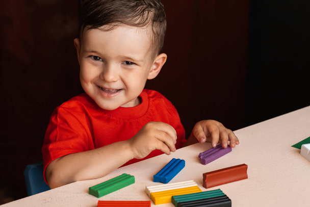 Мальчик делает фигурки из разноцветного пластилина, сидящего за столом. Дошкольное образование. Хобби. Саморазвитие - Фото, изображение