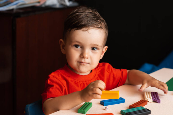 A child boy sculpts figures from multi-colored plasticine sitting at a table. Preschool education. Hobby. Self-development - Photo, Image