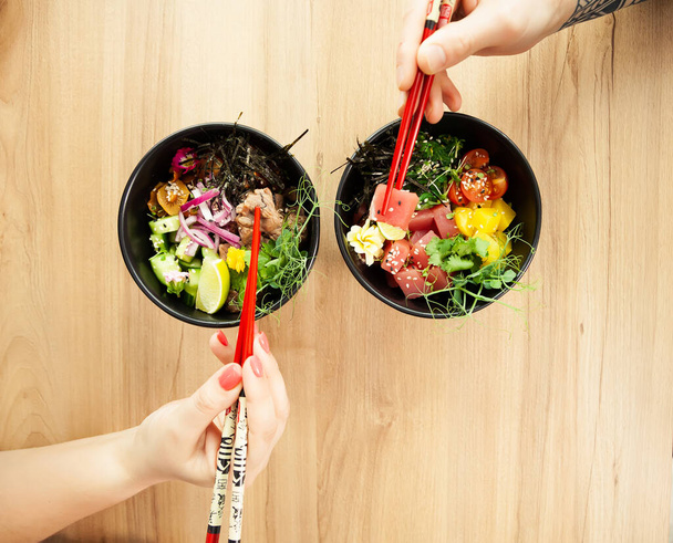 Man and woman eating poke salad with chopsticks. Dab tuna salad in a bowl. People in the restaurant eat salad with chopsticks. Asian seafood salad concept - Fotoğraf, Görsel