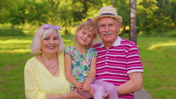Malá roztomilá vnučka objímající s babičkou a dědečkem rodinný pár v parku - Fotografie, Obrázek