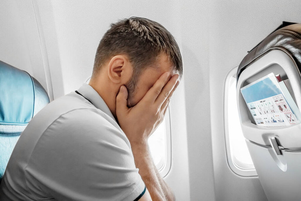 A man sits in front of an airplane window and is nervous, afraid to fly, the cabin of a passenger aircraft. Aerophobia, fobilya, international flights - Φωτογραφία, εικόνα