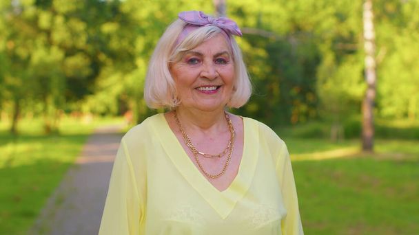 Vrolijke mooie senior oude grijs-harige oma in casual gele blouse op zomer park achtergrond - Foto, afbeelding