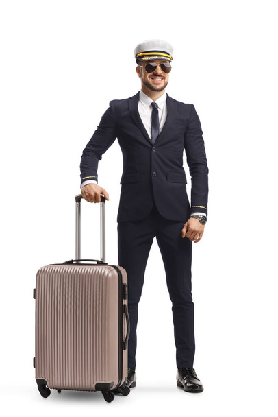 Full length portrait of a young pilot with a suitcase on wheels wearing a uniform and sunglasses isolated on white background - Photo, image