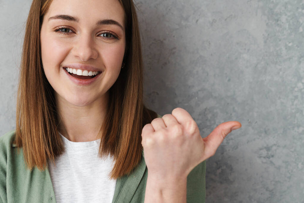 Happy beautiful nice girl smiling and pointing finger aside isolated over grey wall - Foto, Bild