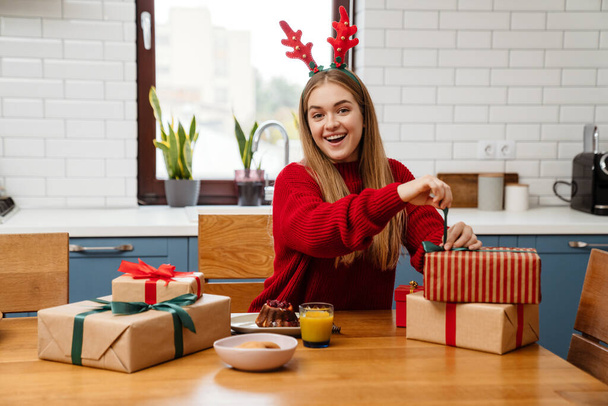 Happy young girl wearing pajamas celebrating christmas at the kitchen table, opening presents - Foto, Bild