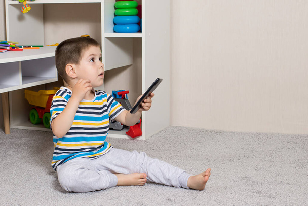 Ein kleines Kind im Alter von 3-4 Jahren und ein Handy im Kinderzimmer mit Platz für Text, um den Raum zu kopieren. Cartoons und die Abhängigkeit von Gadgets bei Kindern, Beschränkung der Kinder von erwachsenen Inhalten auf der - Foto, Bild