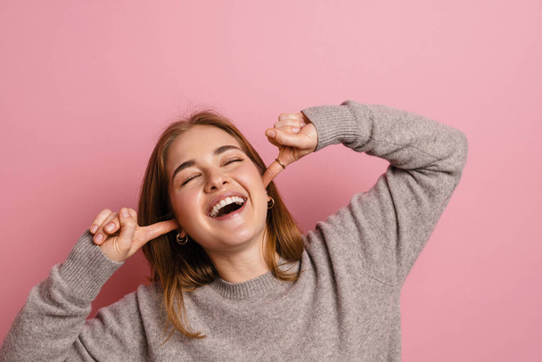Ginger joyful woman laughing while plugging her ears isolated over pink background - Fotoğraf, Görsel