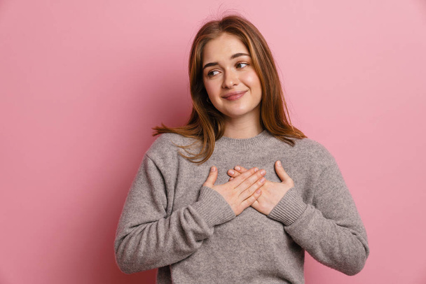 Ginger young happy woman smiling while holding hands on her chest isolated over pink background - Fotoğraf, Görsel