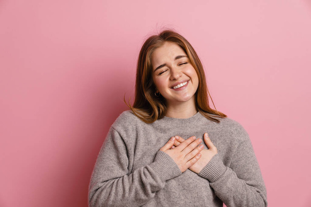 Ginger happy woman laughing while holding hands on her chest isolated over pink background - Fotoğraf, Görsel