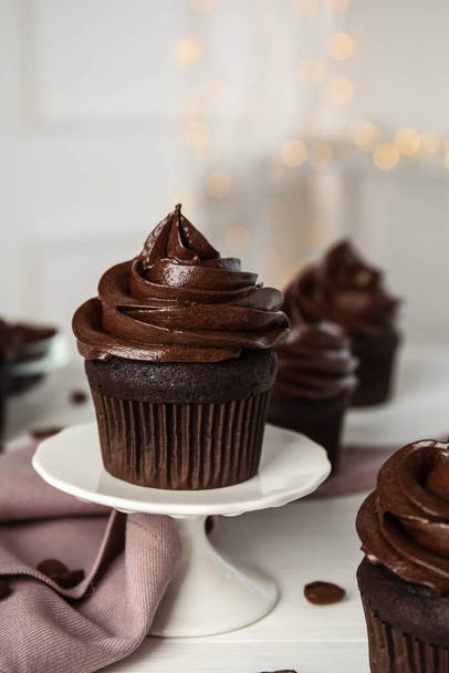 Support à dessert avec délicieux cupcake au chocolat sur table blanche contre les lumières floues - Photo, image