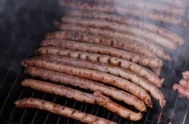 Close up cooking meat sausages on grill, smoking and broiling them, high angle view - Photo, Image
