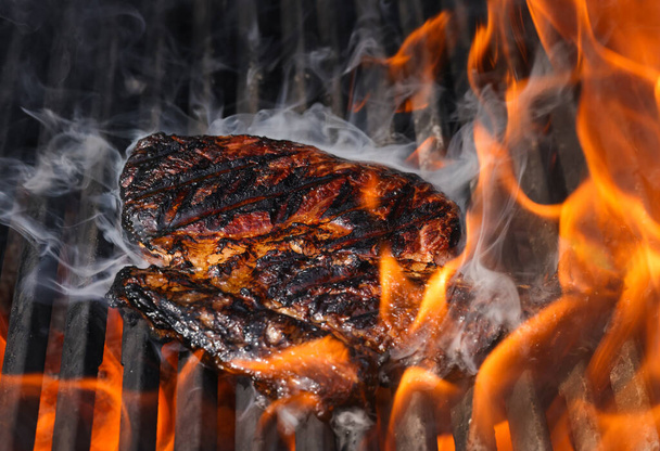 Закрыть сожжение и курение говядины рибай стейки на открытом огне открытый гриль с чугунной металлической решеткой, вид под высоким углом - Фото, изображение
