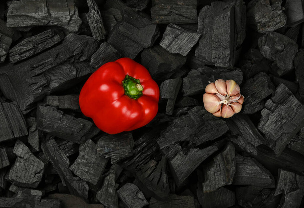 Закрыть сырым красным перцем и чесноком кусочки черного древесного угля, готовые для приготовления гриля на гриле, вид сверху, прямо над - Фото, изображение